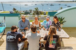 A group of people seated at a wooden table outdoors with a view of boats on the water. - Wanderlust NZ (Tauranga)