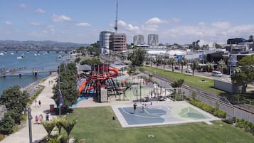 A waterfront park with playgrounds, a basketball court, and a bridge over the water.