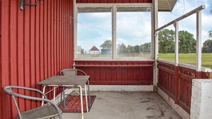 A covered porch with a table and two chairs, a red wall, and a view of a rural landscape. - Awesome home in Everöd with WiFi (Everöd)