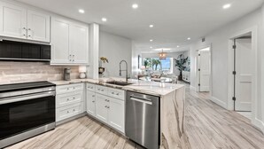 Une cuisine moderne avec des meubles blancs, un lave-vaisselle en acier inoxydable et un plan de travail en marbre.