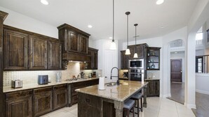 A spacious kitchen with dark wooden cabinets, a large island with bar stools, and modern appliances. - Spacious & Luxe, 5 Star Neighborhood, Movie Theater (Frisco)