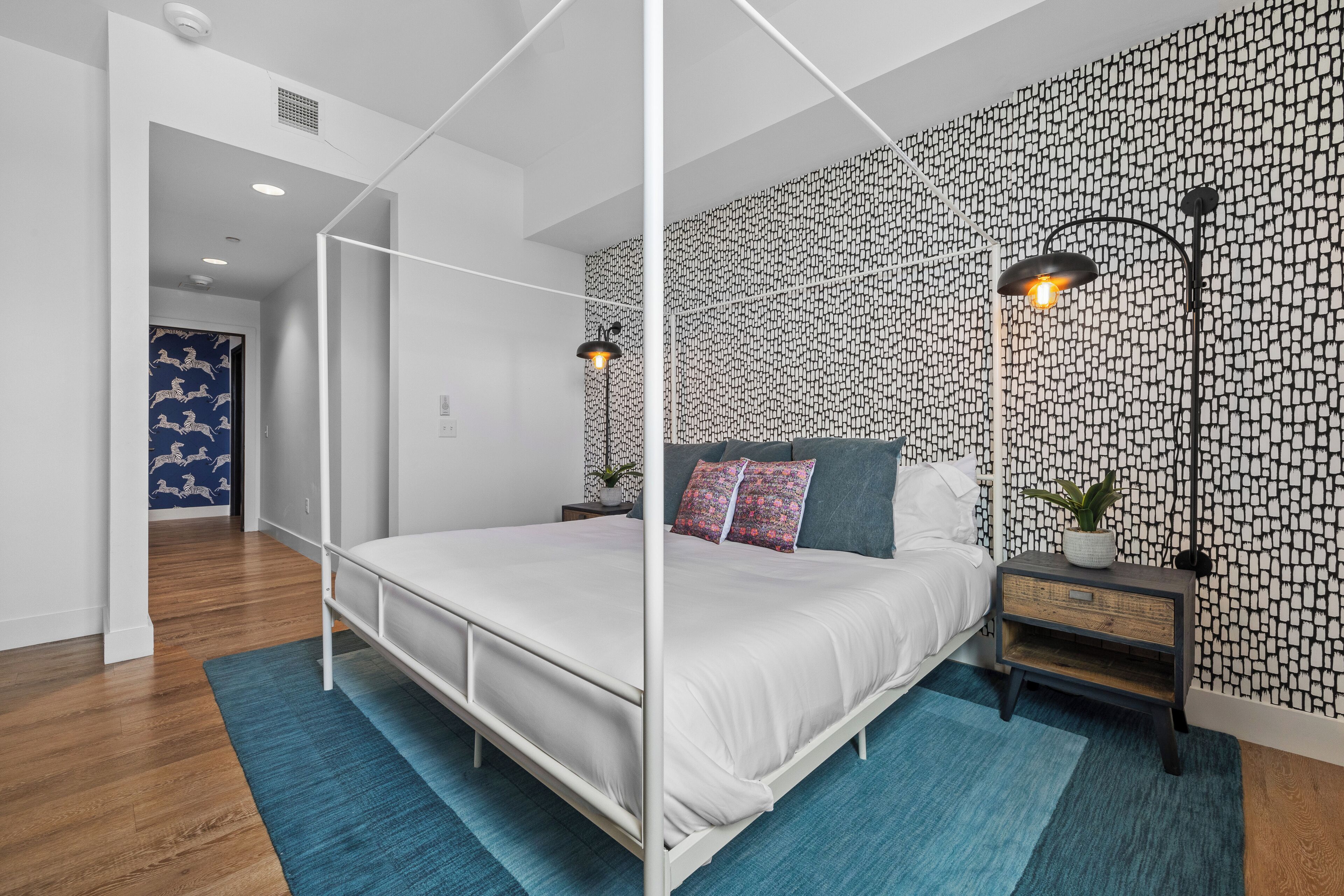 Een moderne slaapkamer met een hemelbed, behang met een patroon en twee bedlampjes.