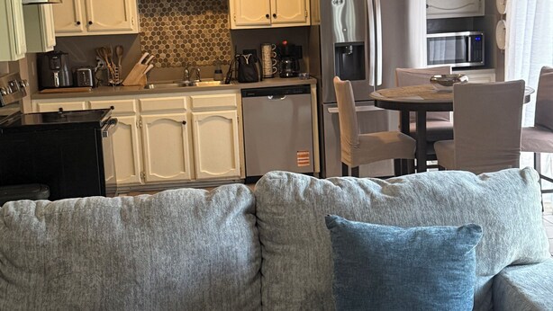 A compact living space with a kitchenette, a dining area, and a sofa with a blue pillow. - This cozy home is a beautiful 3 bedroom, 2 full bathroom as  with a 2-car garage (Baton Rouge)