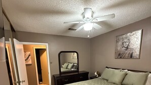A bedroom with a bed, a ceiling fan, a wall-mounted mirror, and a painting. - This cozy home is a beautiful 3 bedroom, 2 full bathroom as  with a 2-car garage (Baton Rouge)