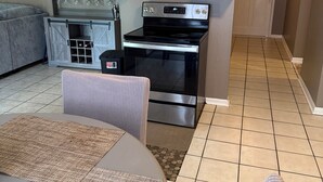 A compact kitchen with a stove, oven, and white cabinets. There is a dining area with a table and chairs. - This cozy home is a beautiful 3 bedroom, 2 full bathroom as  with a 2-car garage (Baton Rouge)