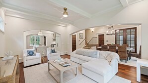 A spacious living room with a white sofa, a coffee table, and a dining area with wicker chairs. - Cypress Point Kiawah, 4 BR, Community Pool, Modern Mediterranean Style! (Kiawah Island)