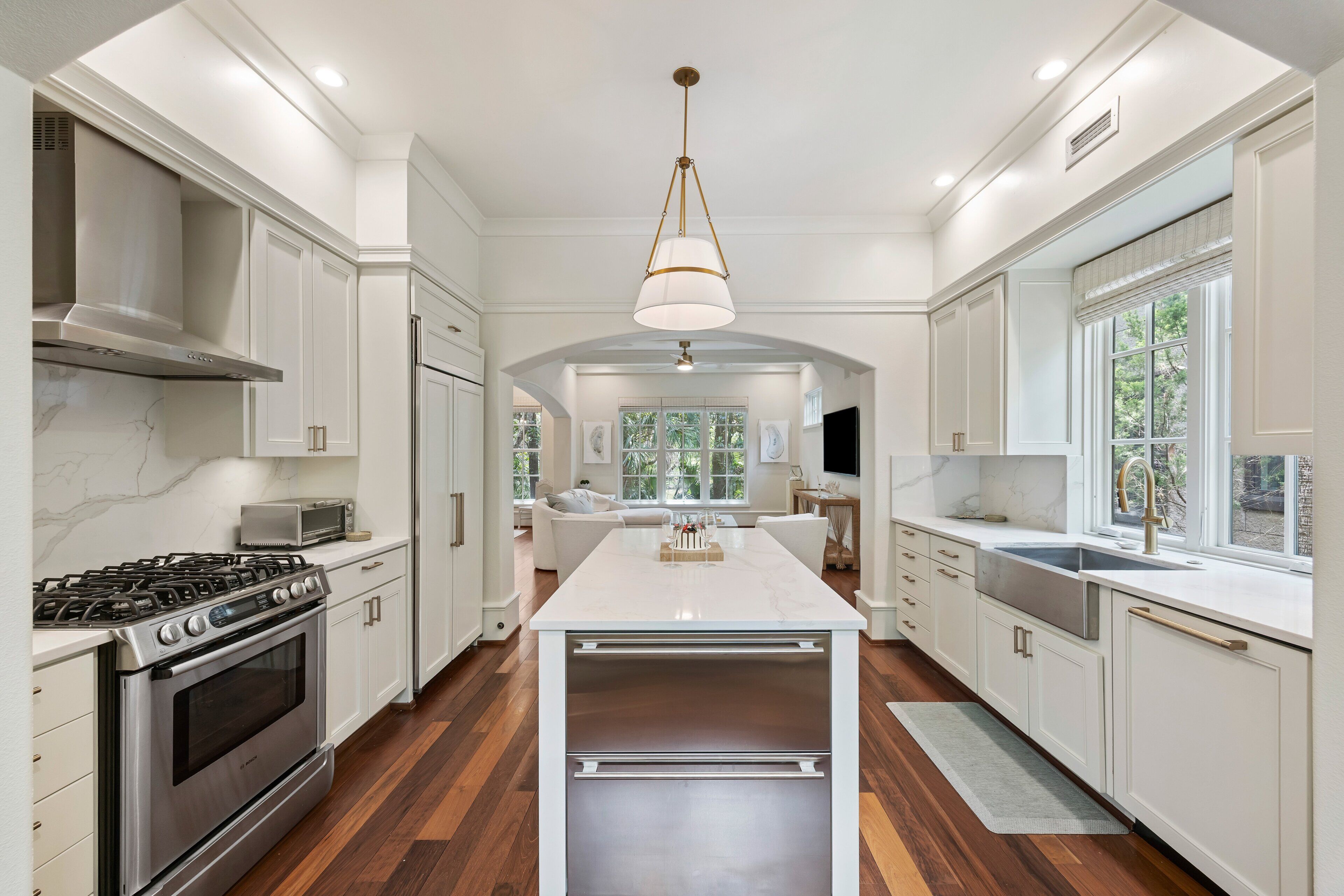 Una cocina moderna con armarios blancos, una isla central, electrodomésticos de acero inoxidable y un amplio ventanal que proporciona luz natural.