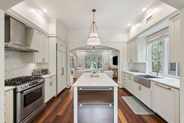 A modern kitchen with white cabinetry, a central island, stainless steel appliances, and a large window providing natural light.