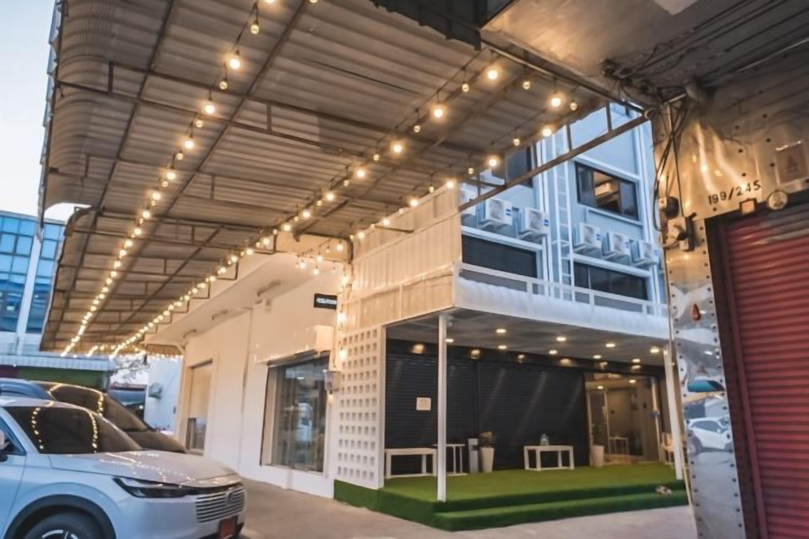 A building with a covered outdoor area, a car parked in front, and a red garage door.