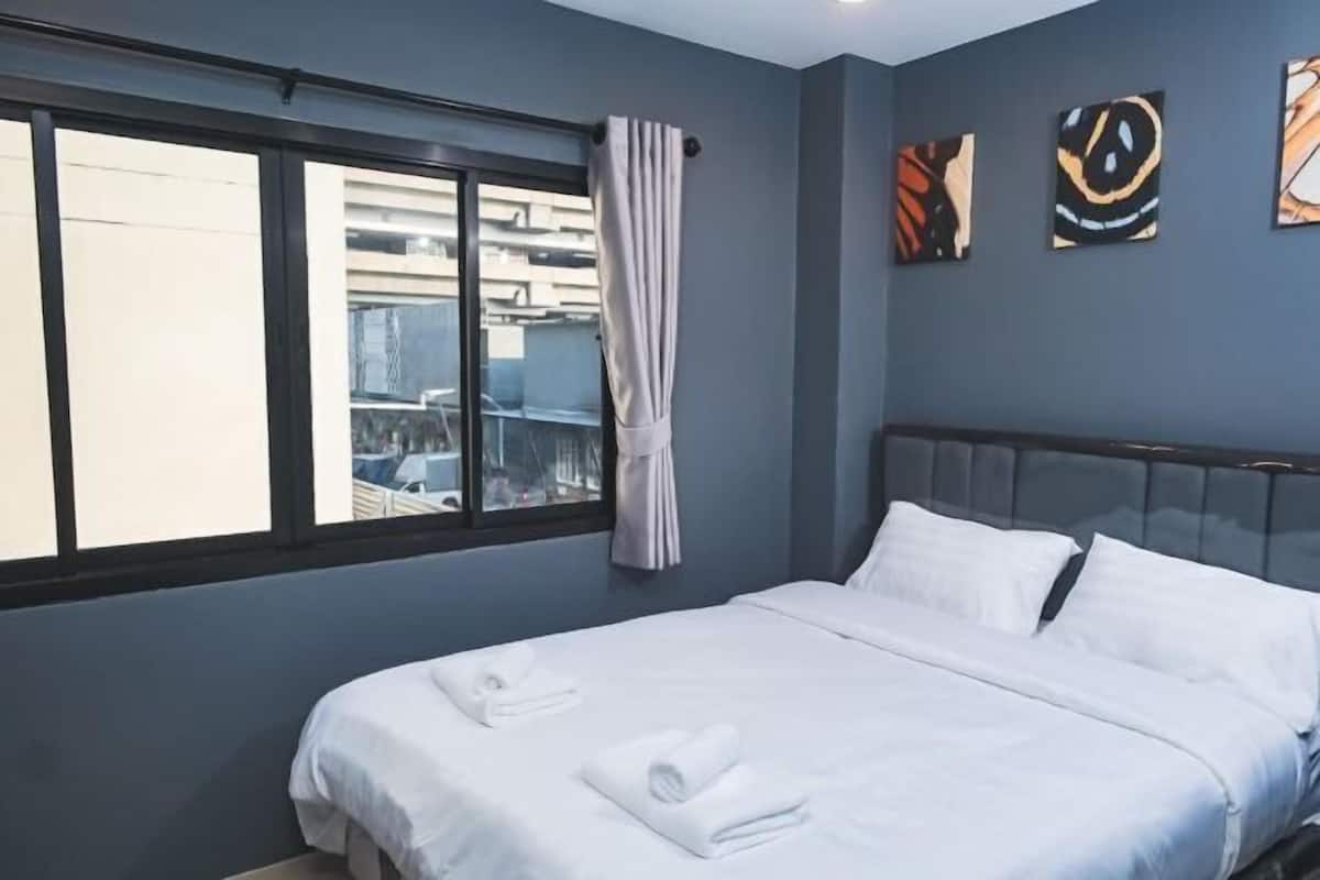 A hotel room with a bed, a window with curtains, and artwork on the wall.