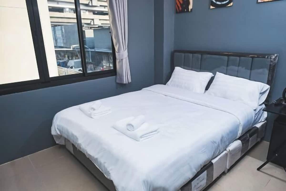 A neatly made bed with white linens and towels, a window with a view of buildings, and a blue wall.