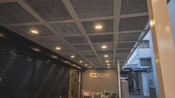 Un pasillo con techo de diseño cuadriculado e iluminación empotrada, que conduce a la entrada de un edificio con un cartel.