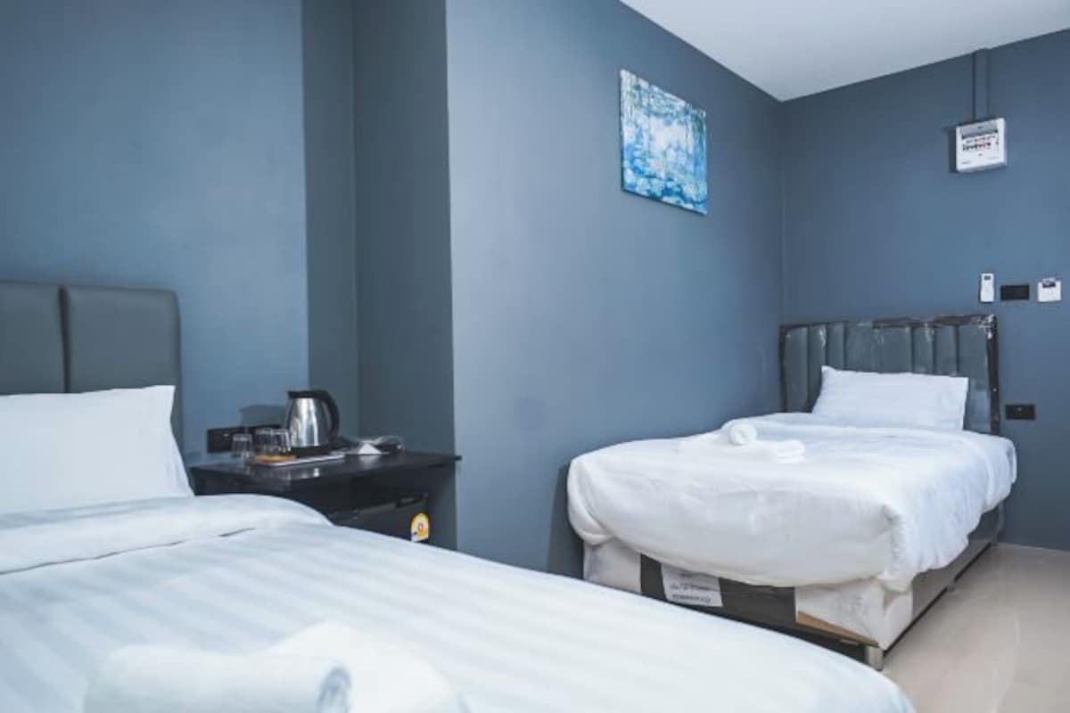 A hotel room with two beds, a nightstand, a painting, and a thermostat.