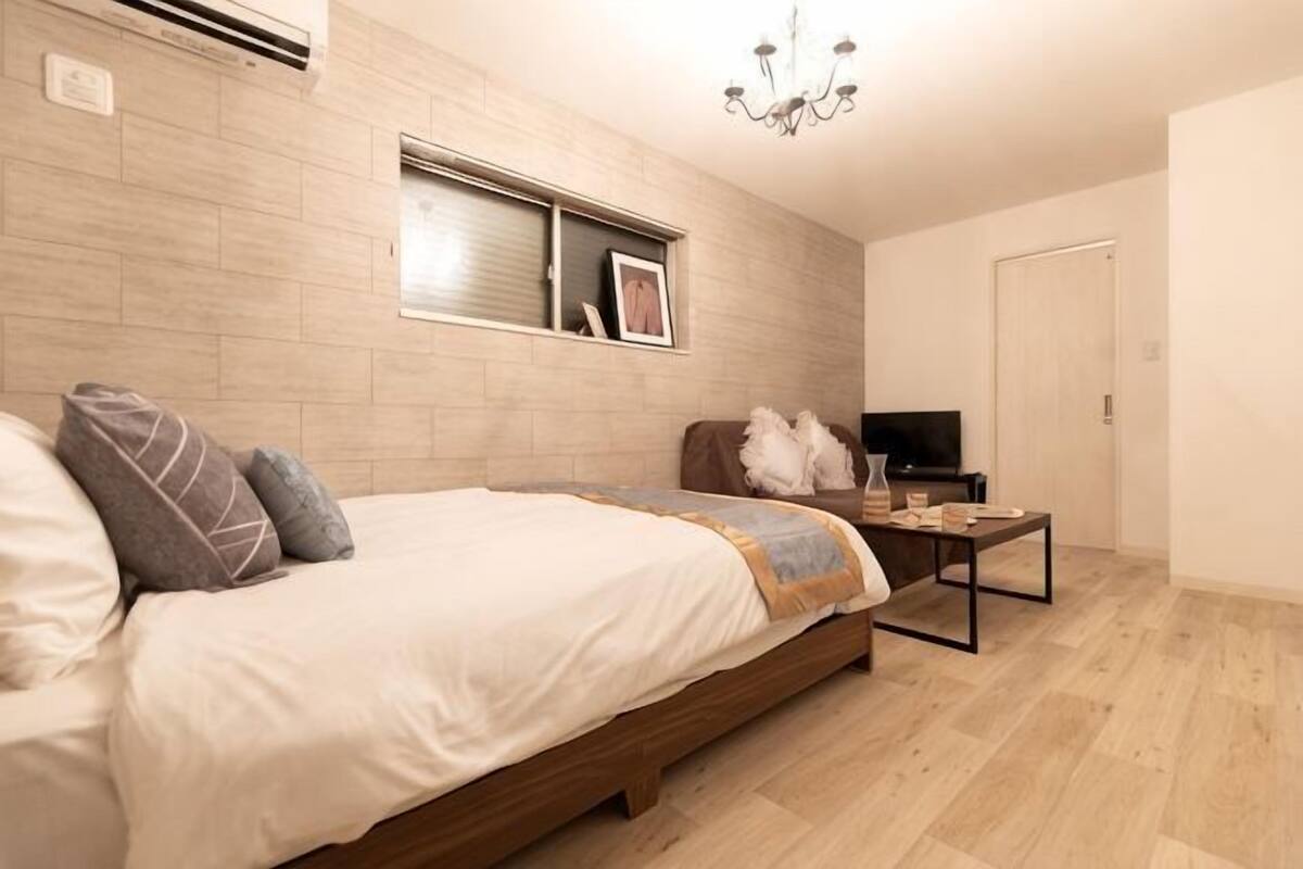 A bedroom with a bed, a bedside table, a TV, and a window.