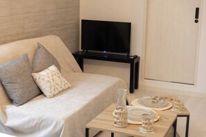 A modern living room with a sofa, a flat-screen TV, and a small table with decorative items. - Tengacyaya Ra Hotel (Osaka)