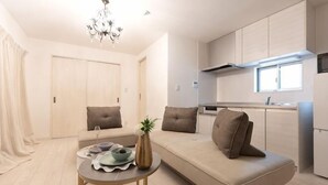 A modern living room with a sofa, a small round table, and a dining area. - Tengacyaya Ra Hotel (Osaka)