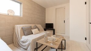 A modern, well-lit room with a sofa, a small table with a vase and a plate, and a television on a stand. - Tengacyaya Ra Hotel (Osaka)