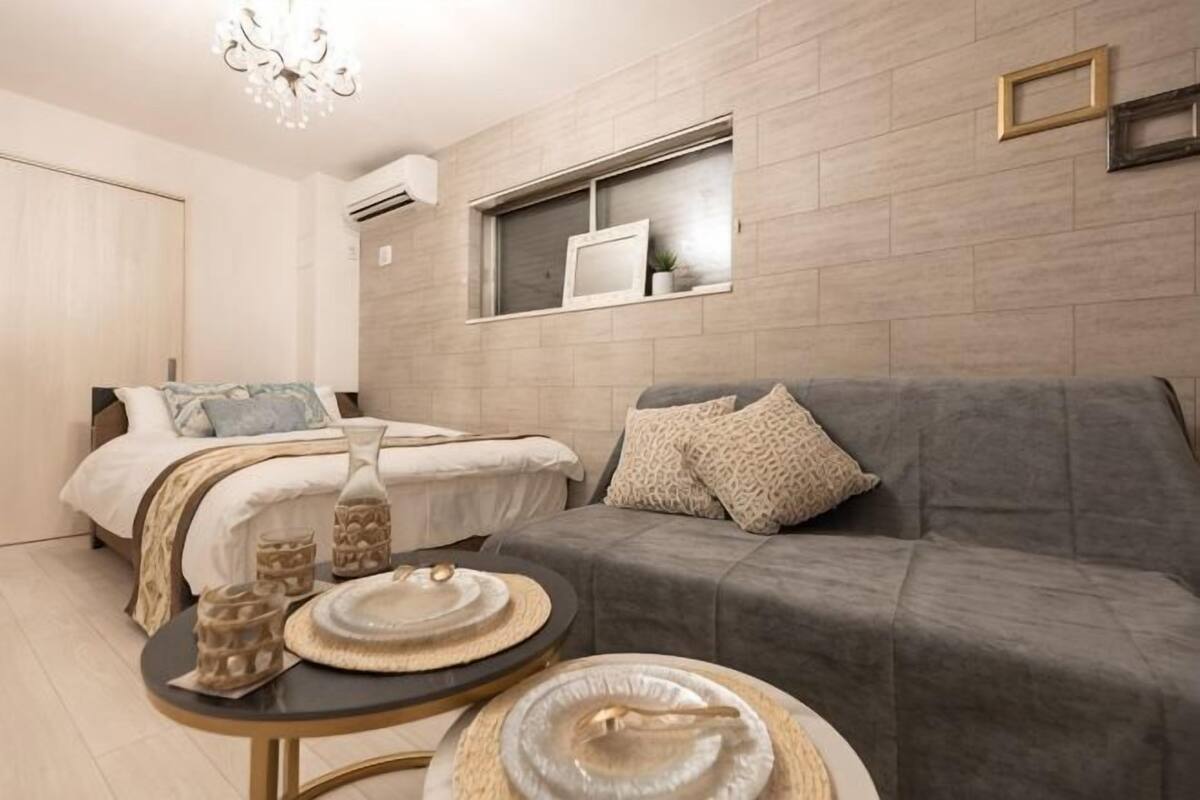 A modern bedroom with a bed, a grey sofa, a small round table with decorative items, and a window with a picture frame.