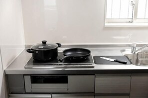 A kitchen with a stove, a frying pan, a pot, and a knife on a counter. - Tengacyaya Ra Hotel (Osaka)