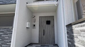 A narrow hallway with white brick walls, a grey door, and a small window. - Tengacyaya Ra Hotel (Osaka)