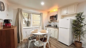 A compact kitchen with white cabinets, a microwave, a refrigerator, and a dining table with chairs.
