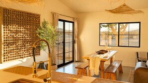 A room with a large window, a dining table, a bench, a chair, and a hanging light fixture. - Sundara | Pool | Spa | Pickleball | Sauna | Games (Joshua Tree)