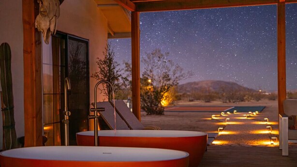 A spa area with two large tubs under a starry sky, a wooden deck, and a desert landscape view. - Sundara | Pool | Spa | Pickleball | Sauna | Games (Joshua Tree)