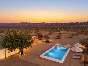 Un paysage désertique avec une piscine, une structure sphérique et un arbre.