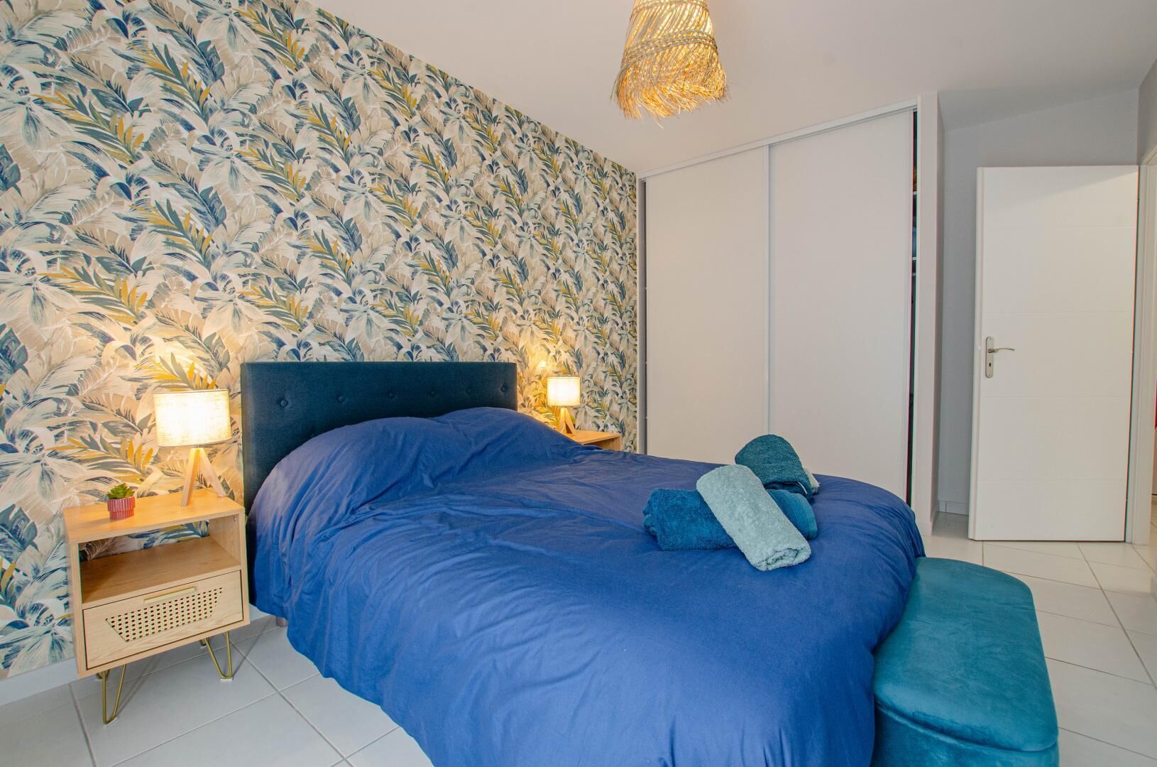 A bedroom with a large bed, two bedside lamps, a nightstand, and a wall with a leafy pattern.