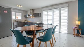A modern kitchen with a dining area, featuring a large round table, teal chairs, and a built-in stove. - Le Fairway - BREVIANDES (BREVIANDES)