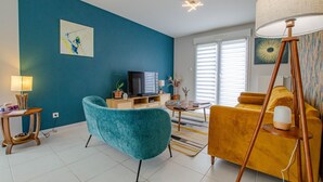A modern living room with teal walls, a yellow sofa, a teal armchair, a wooden coffee table, a TV, and a floor lamp. - Le Fairway - BREVIANDES (BREVIANDES)