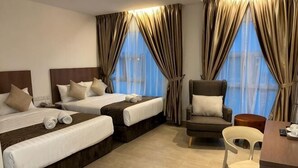 Una camera d'albergo con due letti, una sedia, una scrivania e ampie finestre con tende.