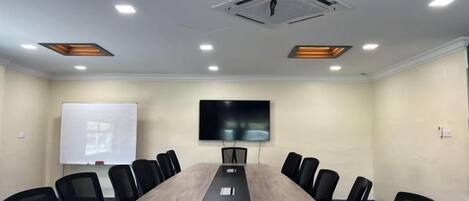 A conference room with a long table, chairs, a projector screen, and a TV.