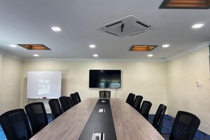 A conference room with a long table, chairs, a projector screen, and a TV. - DSH Hotel (Kuala Kuantan)