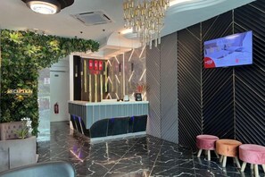 Aula, jossa on vastaanottotiski, televisioruutu ja vastaanottoa ilmoittava kyltti.