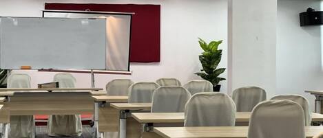 A conference room with a whiteboard, tables, chairs, and a plant.