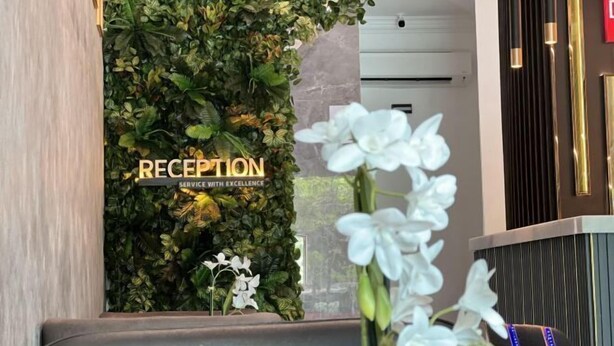 Un'area reception con una parete decorata da verdeggiante vegetazione e un cartello che recita 'RECEPTION SERVICE WITH EXCELLENCE'.