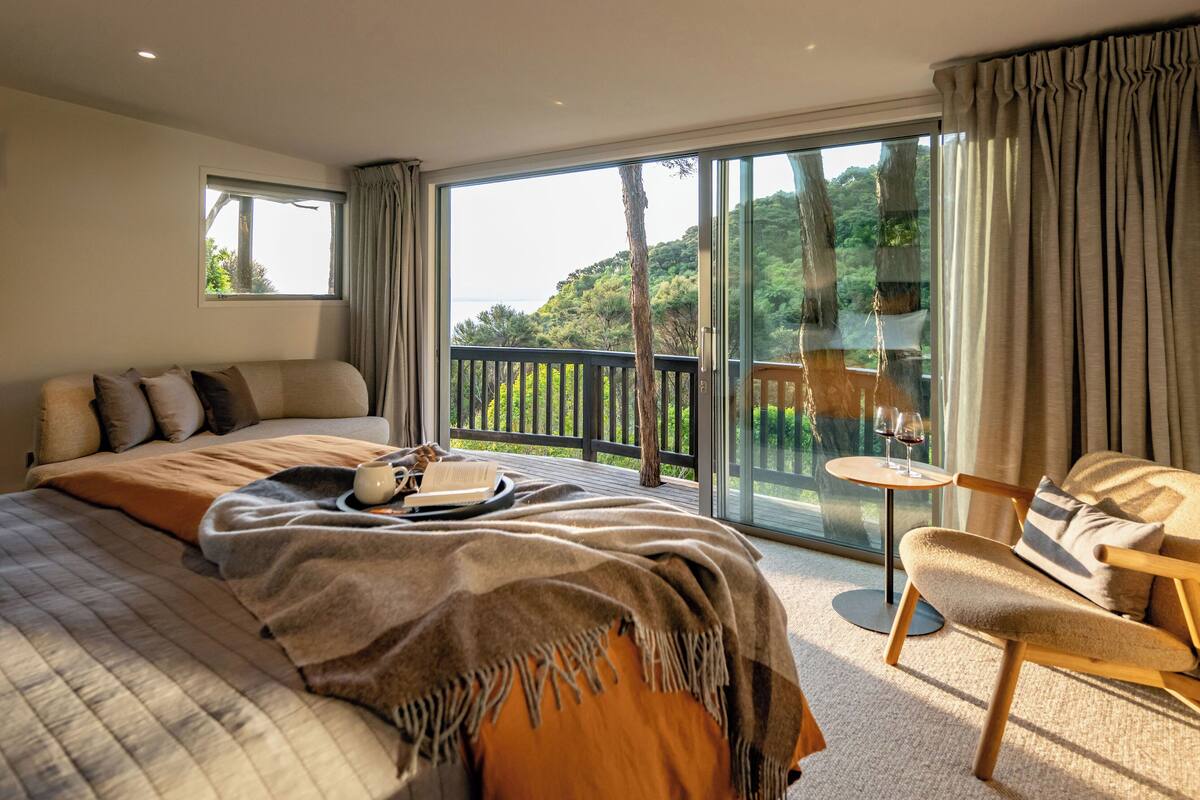 Une chambre avec un grand lit, une petite table sur laquelle reposent deux verres de vin rouge et une chaise.