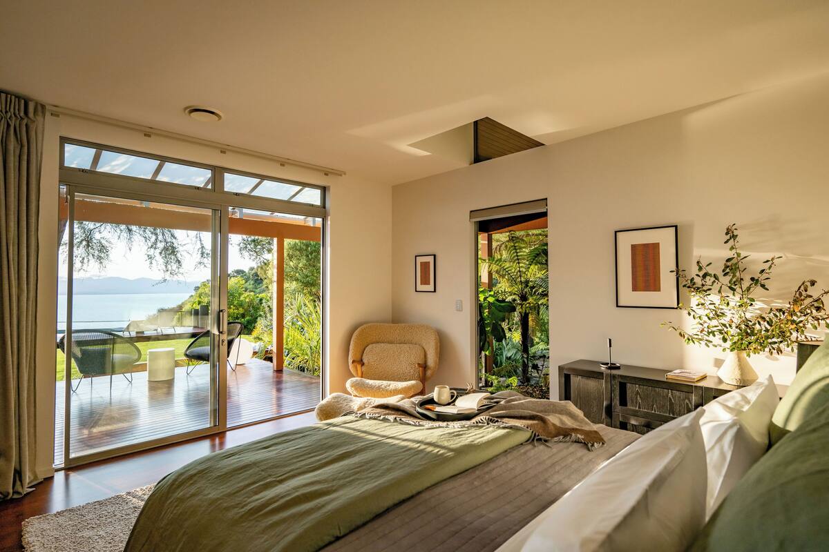 Une chambre avec un grand lit, une chaise, une petite table et une vue sur l’extérieur.
