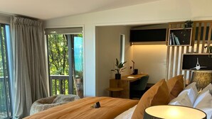 Ein modernes Hotelzimmer mit einem großen Bett, einem Schreibtisch, einem Sessel, einem Fernseher und einem Fenster mit Vorhängen.