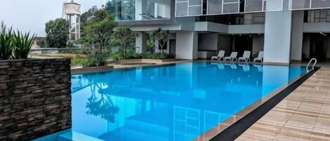 A modern hotel pool area with a clear blue pool, wooden deck, and a glass building in the background.