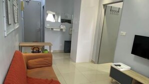 A modern living room with a red sofa, a small table with a kettle, a TV on the wall, and a kitchen area in the background. - Ayuman Suites, Gombak with KL City View (Gombak)