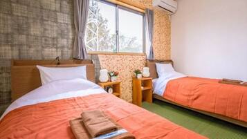 A hotel room with two beds, each with an orange bedspread, a wooden headboard, and a nightstand with a clock and a small plant.