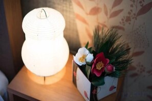 A lit lamp on a wooden surface next to a decorative box with flowers. - Katsushika Takasago House (Tokyo)