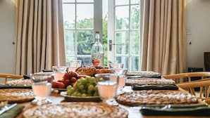 Una mesa de comedor dispuesta con comida y bebidas, una botella de Bowlet, y vistas a la vegetación a través de grandes ventanales.