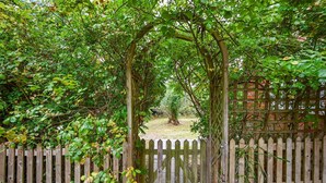Un portón de madera que da a un jardín con un muro de ladrillo y una cerca de madera.