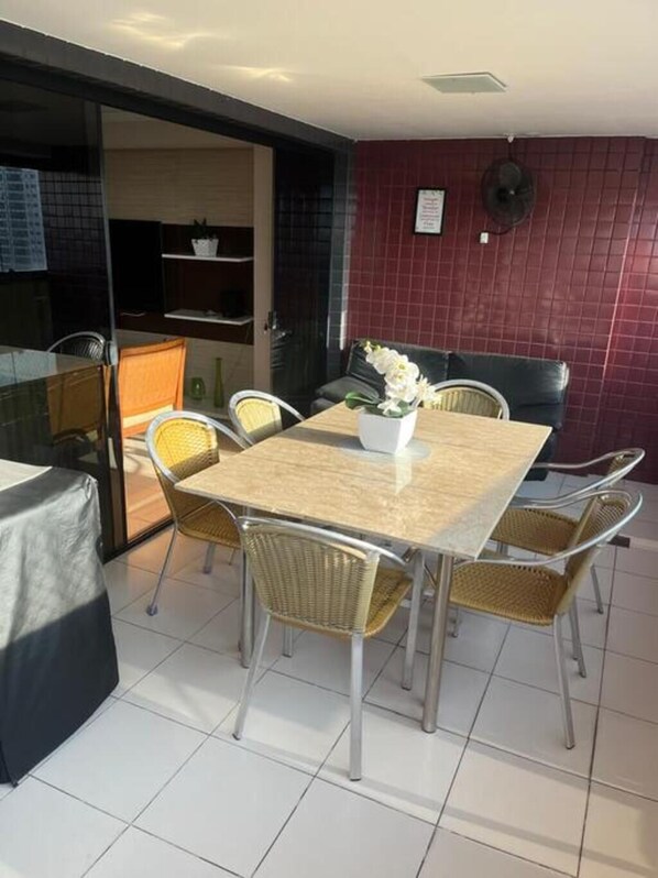 Un coin repas avec une table et des chaises, un ventilateur et un mur recouvert de carreaux rouges.