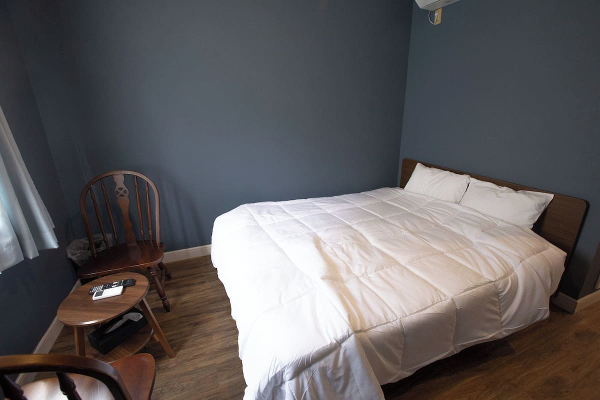 Un dormitorio con cama, una silla, una mesita y un ventilador de techo.
