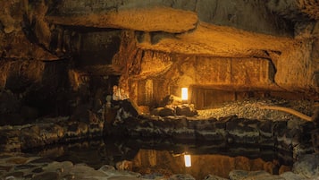 A cave interior with a central hut-like structure, a reflective water surface, and a cave wall.