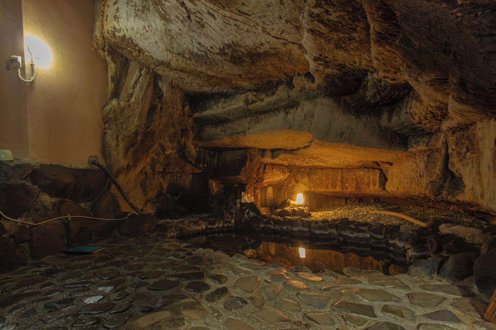 Interior de una cueva con suelo de piedra, techo de paja y una fuente de luz.